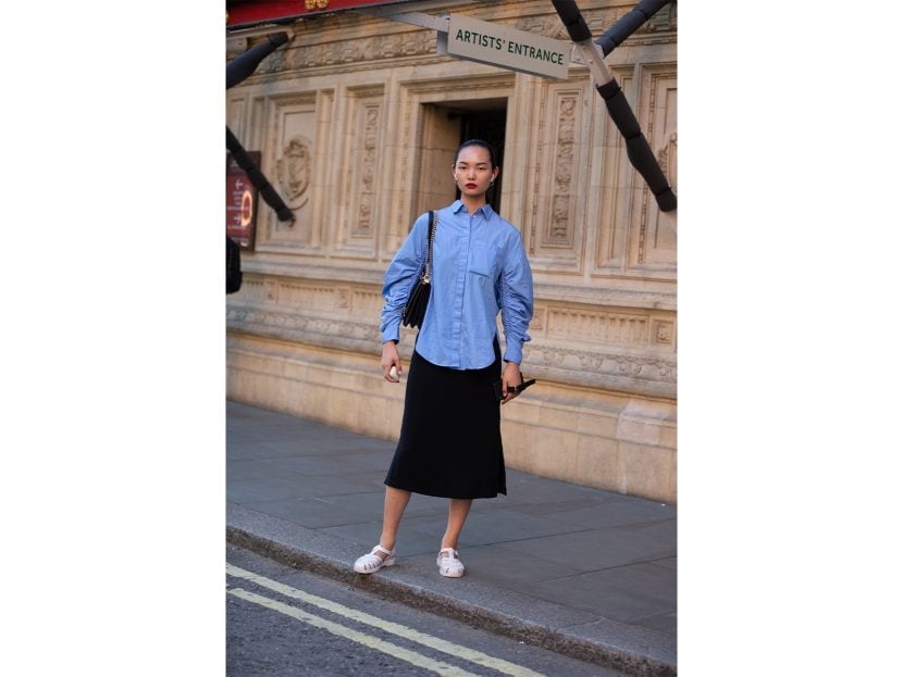 Model Ling Chen wears Airpods, a blue blouse, black skirt, and light pink jelly sandals after the Emilia Wickstead show during London Fashion Week September 2019 on September 15, 2019 in London, England